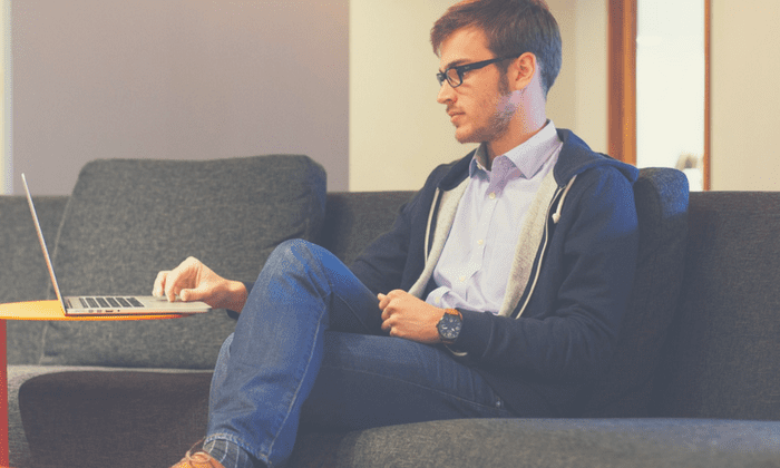 man sitting on couch looking at laptop