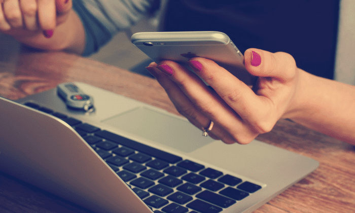 woman holding smartphone over laptop